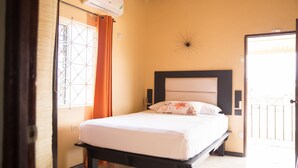 A bedroom with a bed, a window with curtains, an air conditioning unit, and a decorative wall piece. - Apartment in Hellshire near Beach (Hellshire)