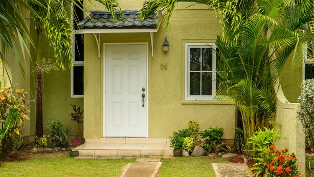 A house with a white door, number 94, surrounded by lush greenery and a well-maintained lawn.