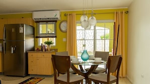 A kitchen with a stainless steel refrigerator, wooden cabinets, a dining table with chairs, and a window with curtains.
