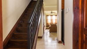 A wooden staircase leading to a living area with a ceiling fan, a refrigerator, and a door with a wooden frame. - Kinsgton Modern Duplex Apartment with Pool (Kingston)