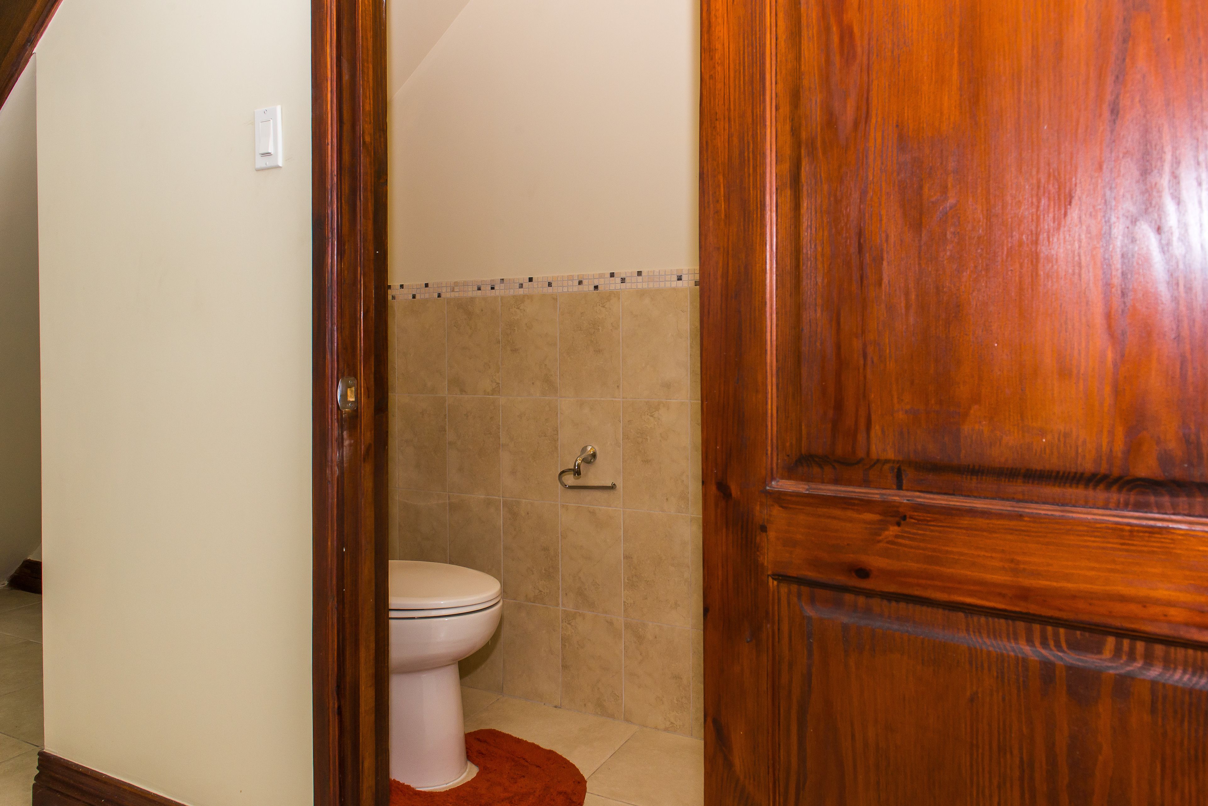 Une salle de bain avec des toilettes, une porte en bois et des murs carrelés.