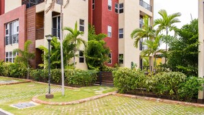 A residential building with a red and beige facade, multiple balconies, and a well-maintained garden with palm trees and shrubs. - Kinsgton Modern Duplex Apartment with Pool (Kingston)