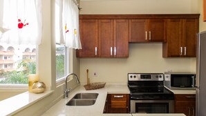 A kitchen with wooden cabinets, a stainless steel sink, a microwave, and an oven. - Kinsgton Modern Duplex Apartment with Pool (Kingston)