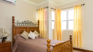 A neatly made bed with a wooden headboard, a nightstand with a vase of flowers, and a window with curtains. - Kinsgton Modern Duplex Apartment with Pool (Kingston)