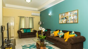 A living room with two brown sofas, a glass coffee table, a TV, and a painting on the wall.