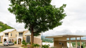A hotel with a covered outdoor seating area, a large tree, and a view of the surrounding landscape. - City Ridge Luxury Penthouse (Kingston)
