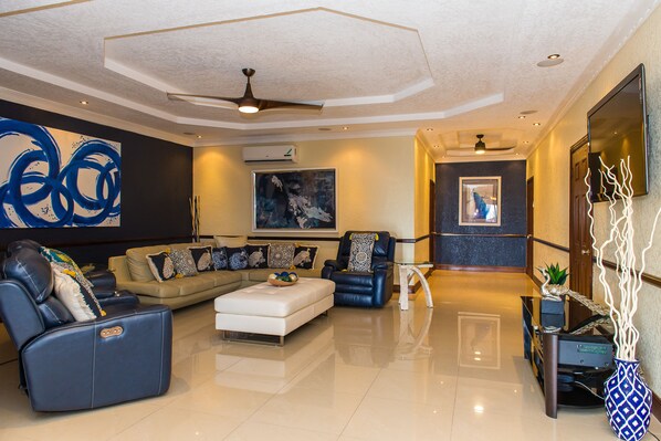 A modern living room with a sofa, a recliner, and a coffee table. There is a painting on the wall and a ceiling fan. - Kingston Luxury Family Retreat (Kingston)