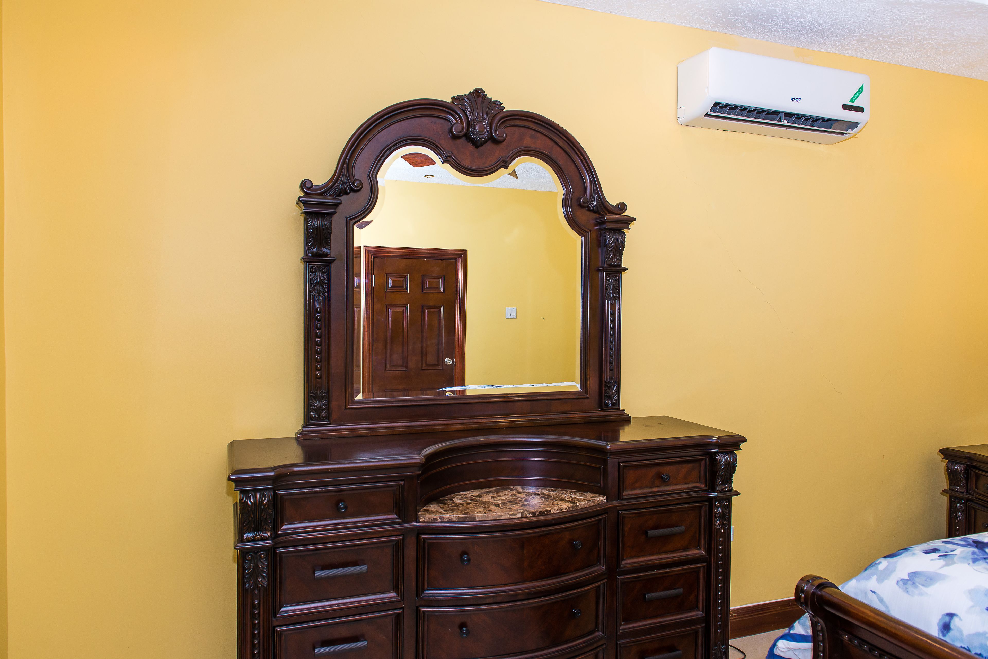 A bedroom with a wooden dresser, a large mirror, and a bed with a floral bedspread.