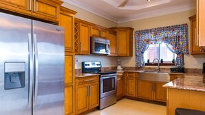 Een keuken met houten kastjes, roestvrijstalen apparatuur, een koelkast, magnetron, oven en een spoelbak.