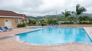 A swimming pool with blue water, surrounded by lounge chairs and a building with a brown roof. - Ocho Rios Beach House at Dax Hall (Ocho Rios)