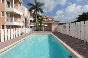 A swimming pool with a white fence, a building with balconies, and palm trees. - Kgn Most Centrally Located One Bdrm II (Kingston)