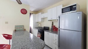 A kitchen with white cabinets, a granite countertop, a stainless steel refrigerator, a microwave, a stove, and a red clock on the wall. - Kgn Most Centrally Located One Bdrm II (Kingston)