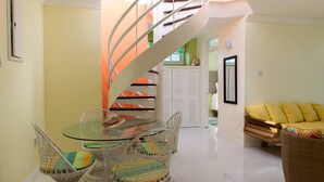 Un interior moderno con una mesa de comedor de vidrio, sillas de mimbre, una escalera en espiral y un sofá amarillo.