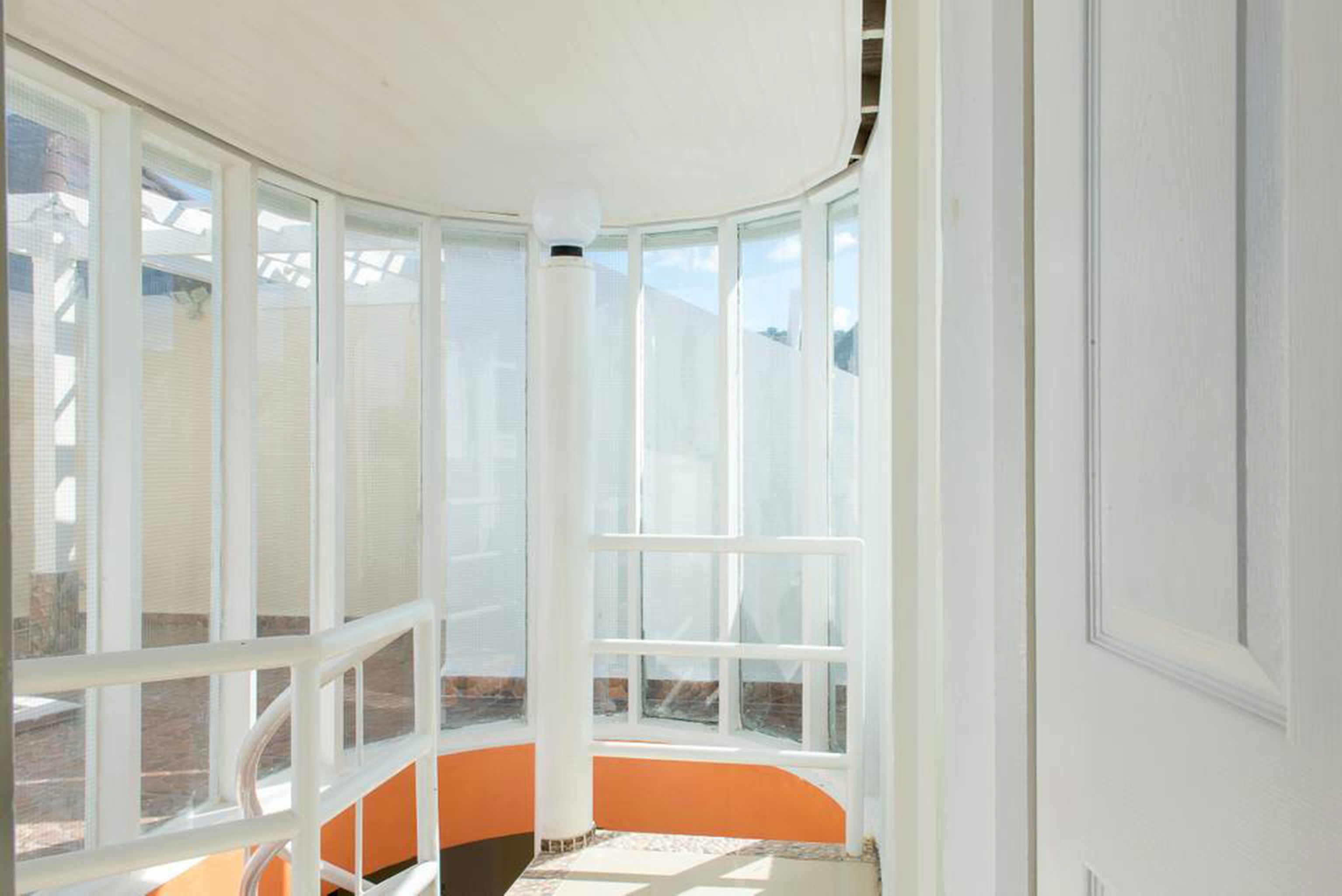Una habitación con ventanas amplias, techo blanco y paredes anaranjadas.