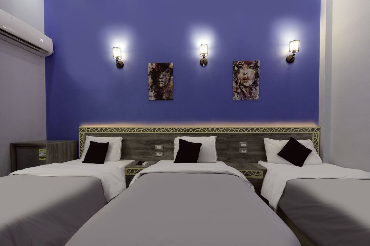 A hotel room with two beds, a headboard with a geometric pattern, and wall-mounted light fixtures.