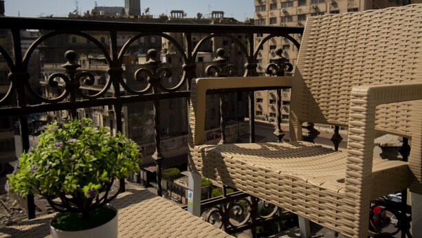 A balcony with a wicker chair, a potted plant, and a view of the cityscape. - Australian Deluxe Hostel (Cairo)