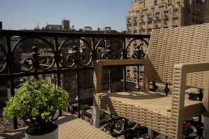 A balcony with a wicker chair, a potted plant, and a view of the cityscape. - Australian Deluxe Hostel (Cairo)