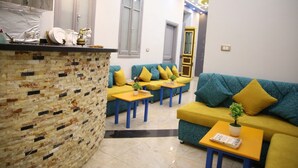 A modern living area with a brick accent wall, a sofa set with yellow cushions, and a small table with a plant. - Australian Deluxe Hostel (Cairo)