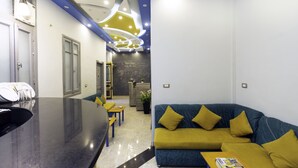 A modern interior with a black reception desk, a blue sofa with yellow cushions, and a chalkboard wall with writing. - Australian Deluxe Hostel (Cairo)