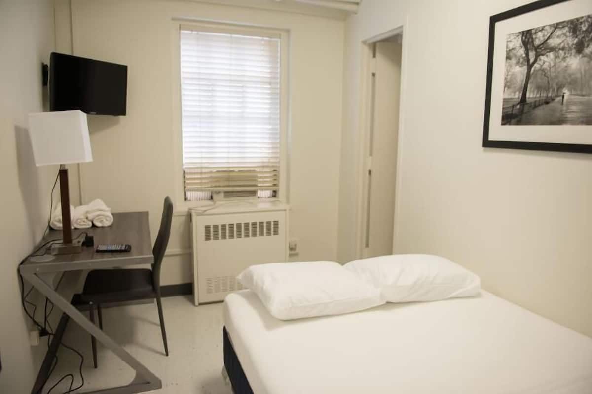 A hotel room with a bed, a desk with a chair, a TV, and a radiator.