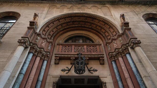 An ornate building entrance with a detailed archway and a coat of arms above the door.