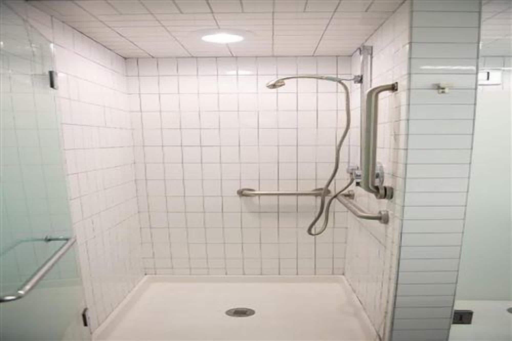 A shower area with white tiled walls, a glass shower enclosure, and a metal grab bar.