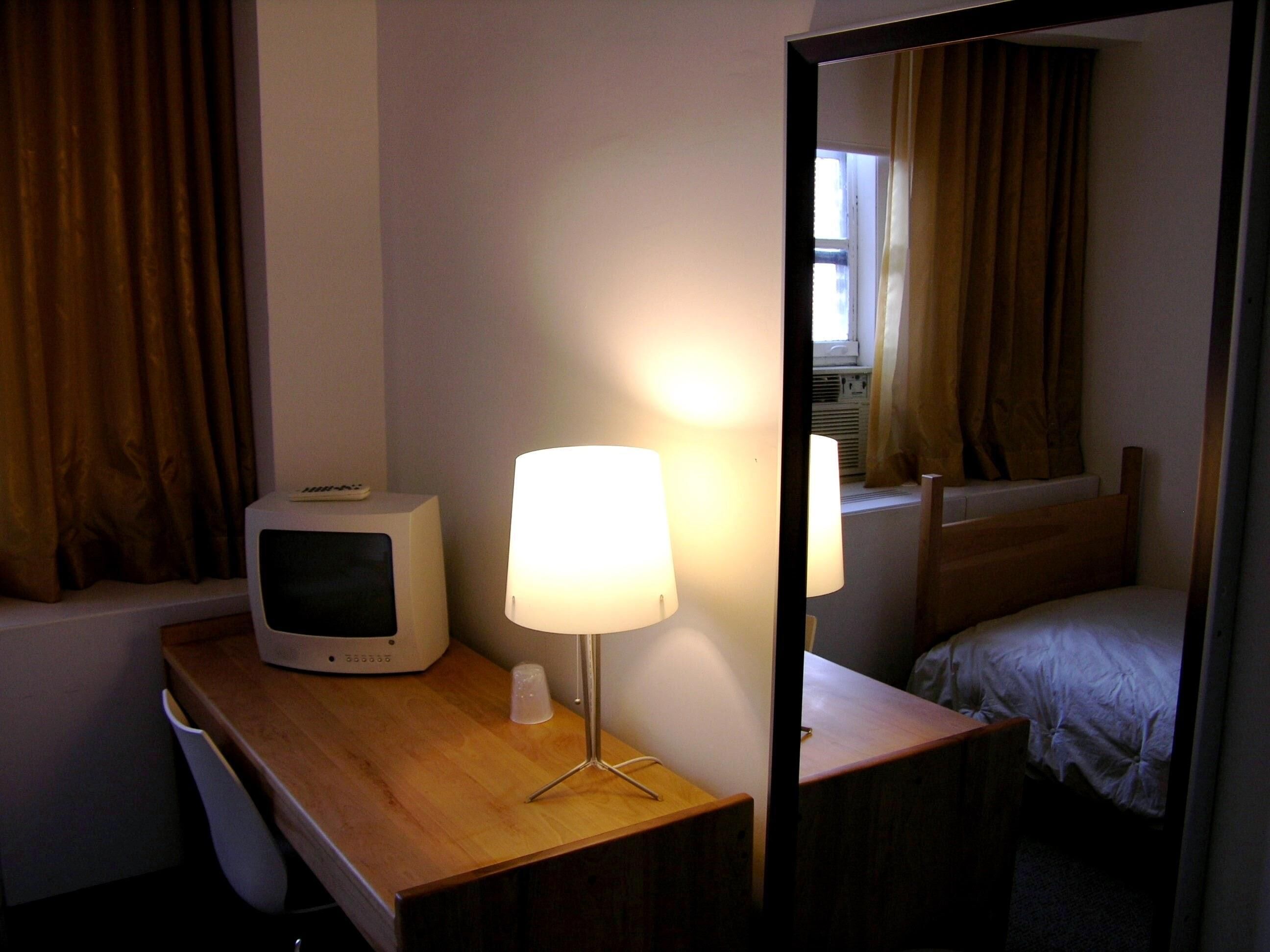 A hotel room with a wooden desk, a television, a lamp, and a bed.