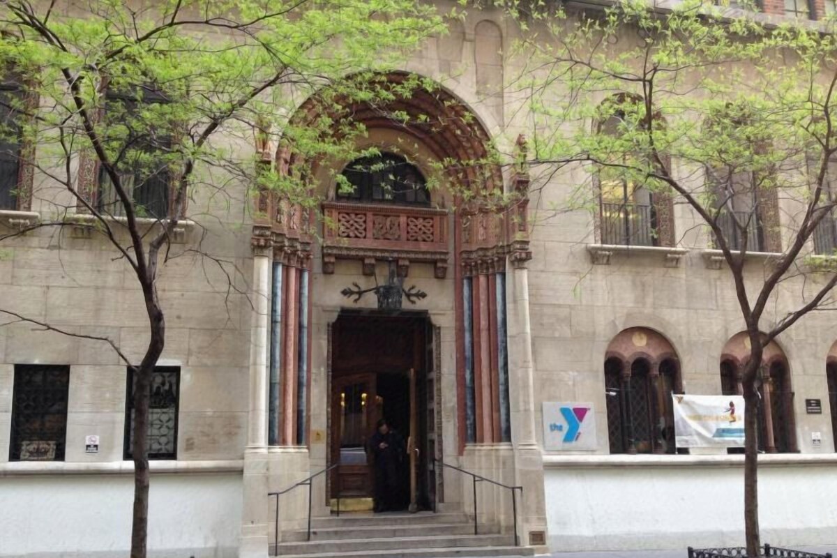A building with an arched entrance, a staircase leading up to it, and a tree in front.