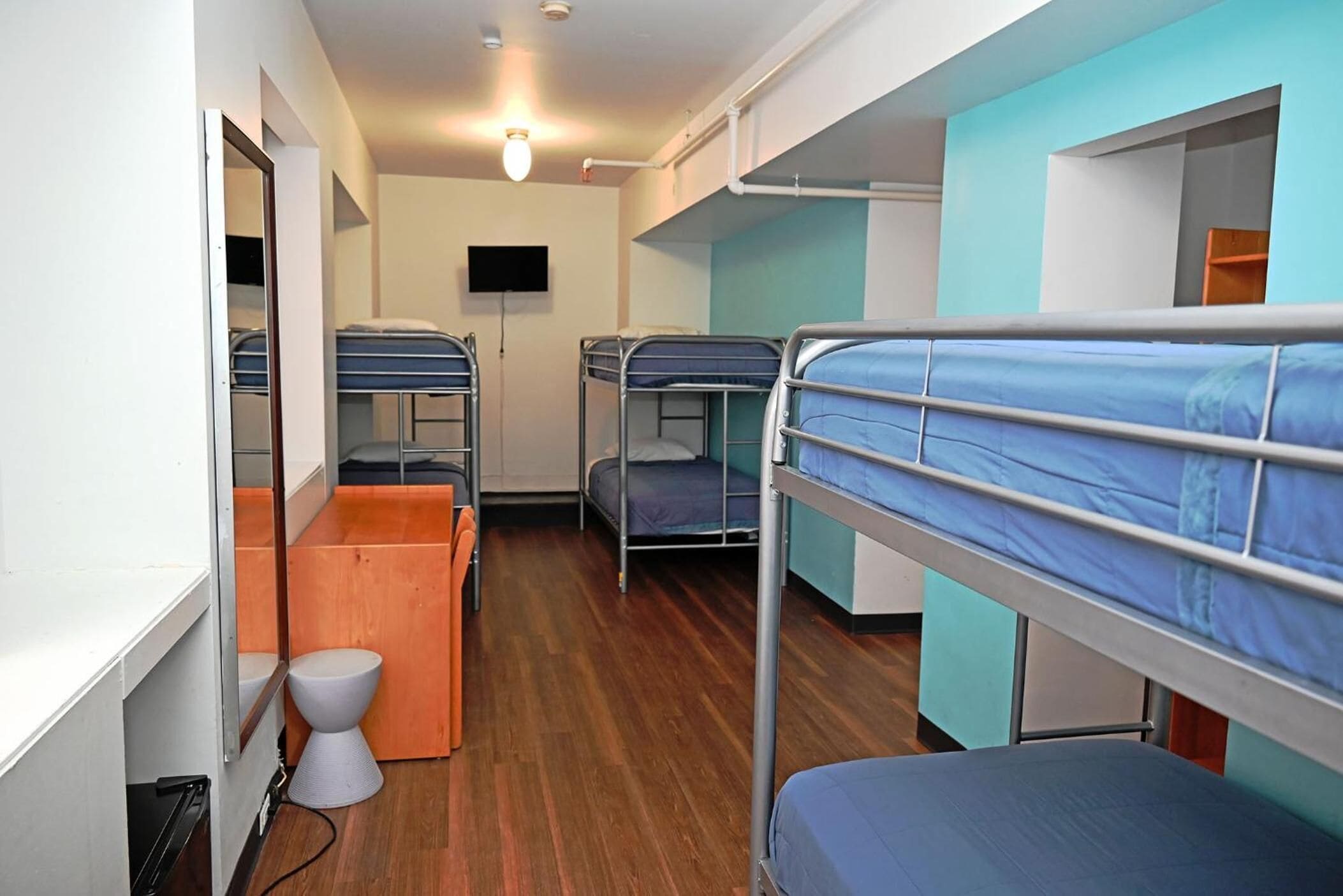 A dormitory room with bunk beds, a small wooden desk, a white toilet, and a television on the wall.
