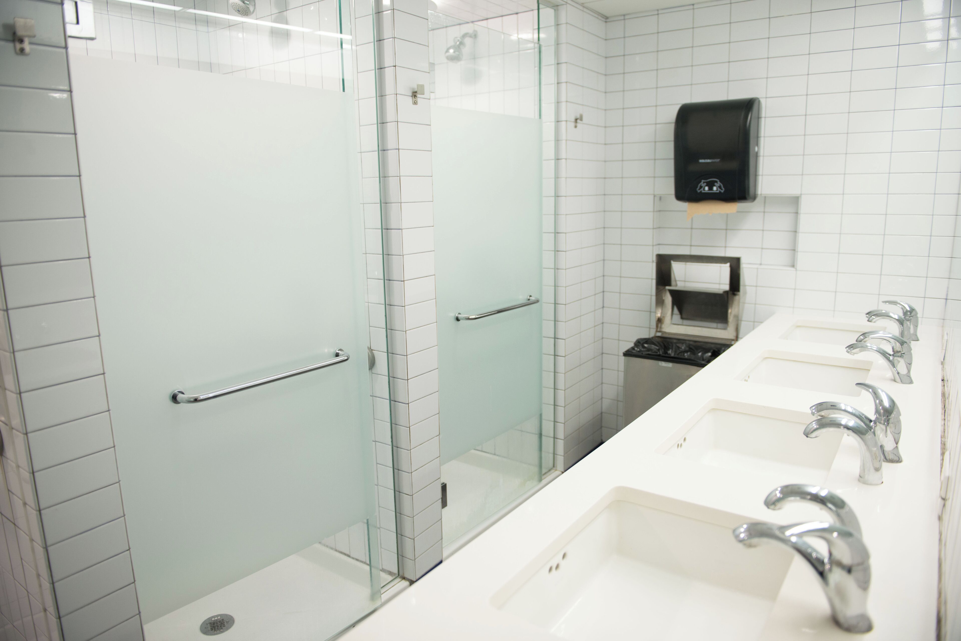 Een moderne badkamer met een douchecabine van glas, een handdroger en een rij wastafels met kranen.