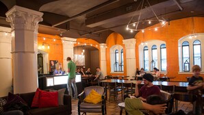 A spacious indoor area with high ceilings, arched windows, and a mix of seating arrangements including tables and chairs.