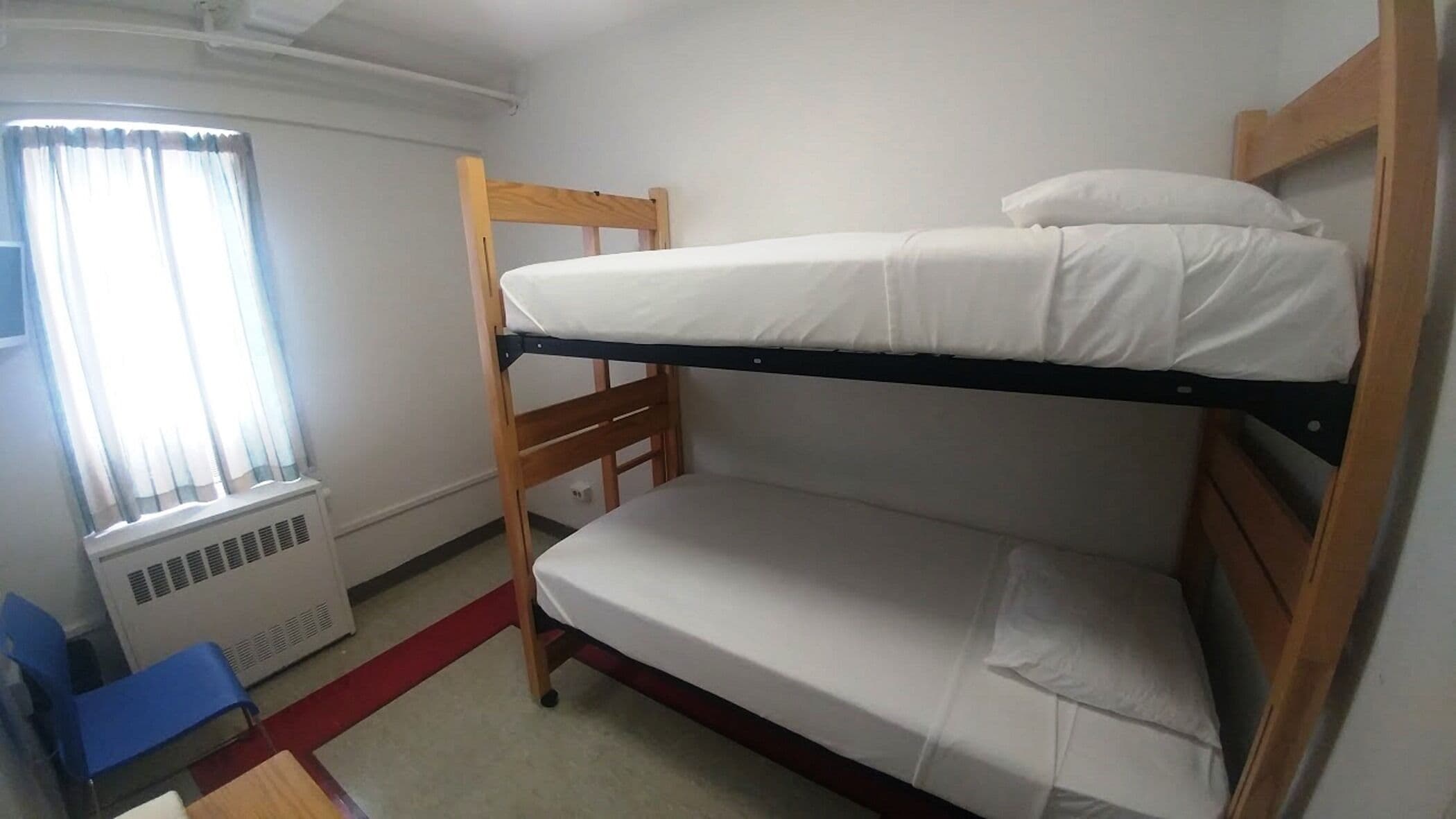 Une chambre avec un lit superposé, une fenêtre, un radiateur et une chaise bleue.