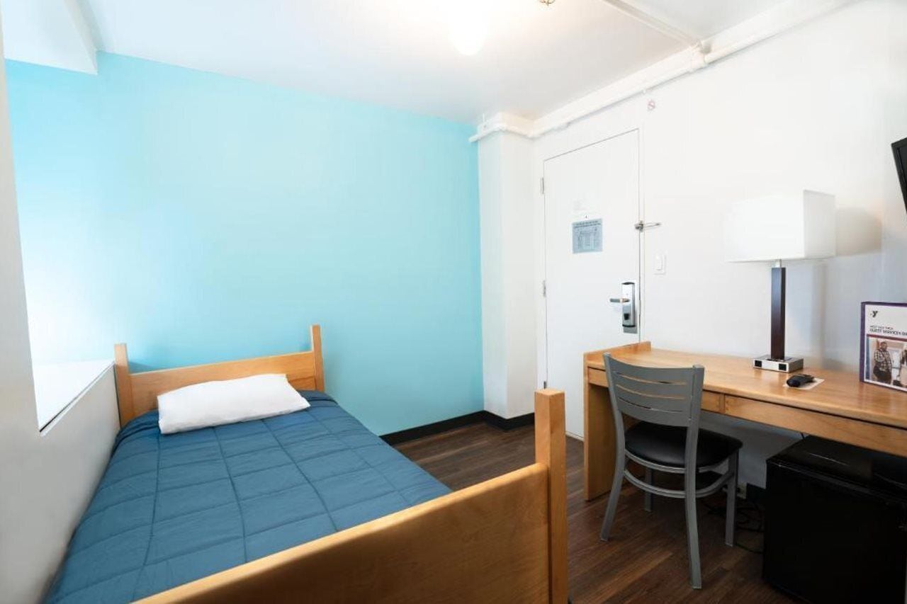 Una habitación pequeña y limpia con una cama individual, un escritorio y una silla.