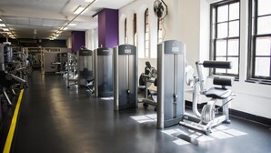 A gym with various exercise machines, a fan, and large windows allowing natural light.