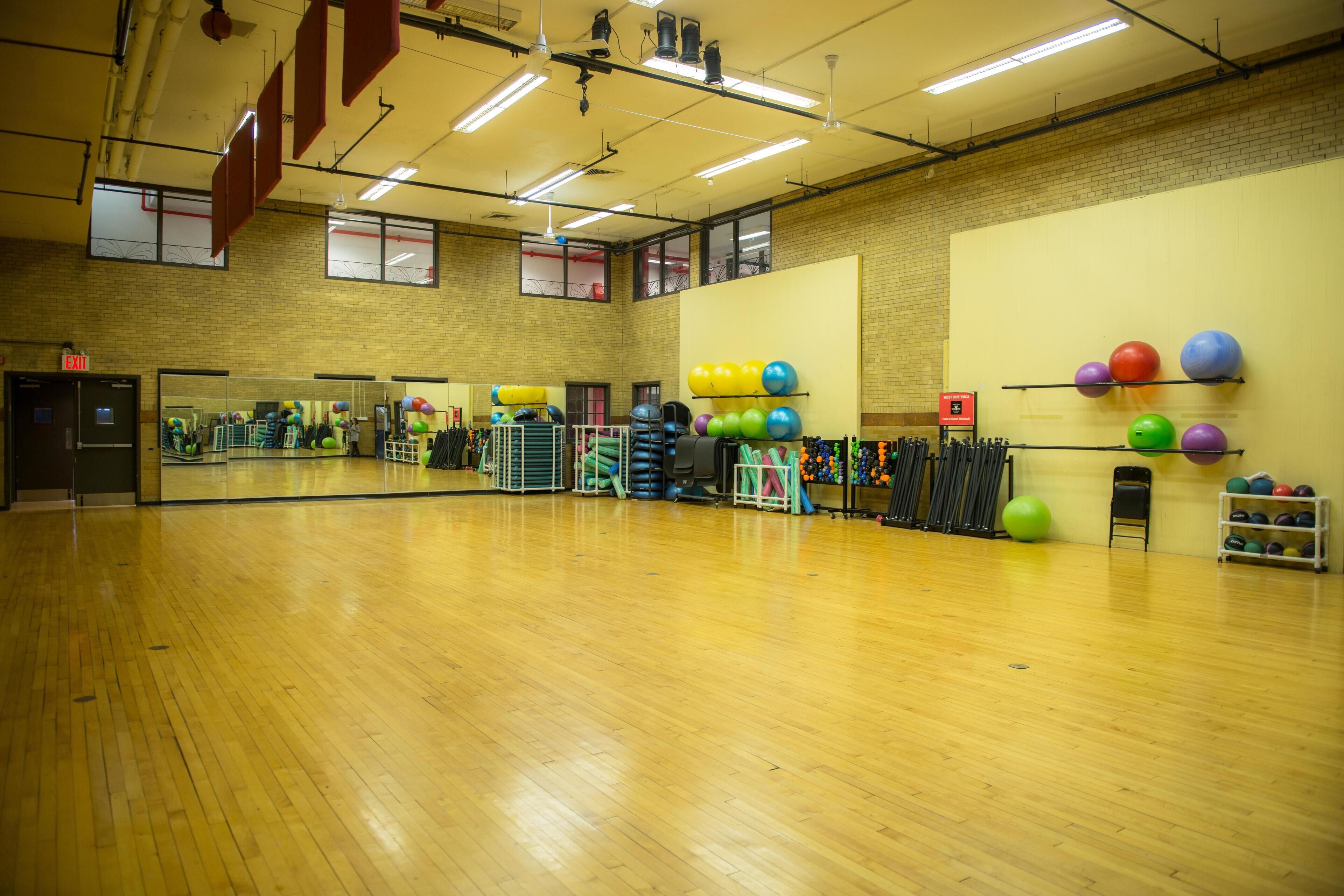 A spacious gym with wooden floors, exercise equipment, and a large mirror.