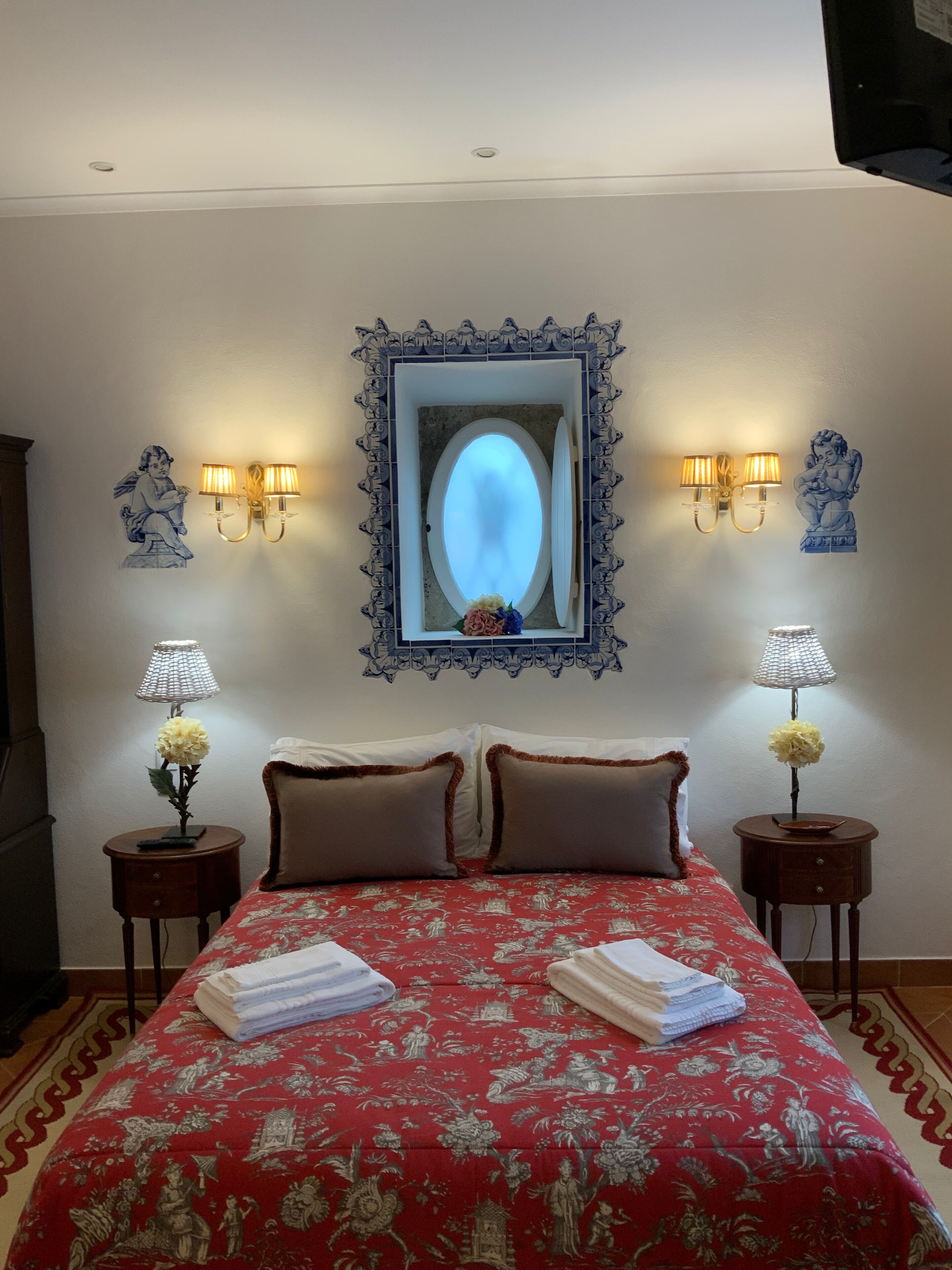 Habitación de hotel con una cama grande, dos mesitas de noche con lámparas, un espejo decorativo y apliques de pared.