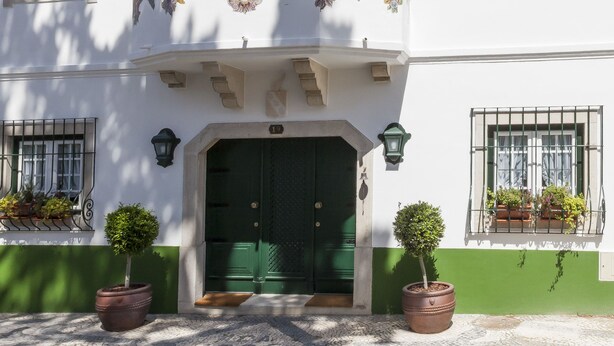 Un edificio tradicional con una puerta verde, paredes blancas y un balcón con barandillas ornamentales.