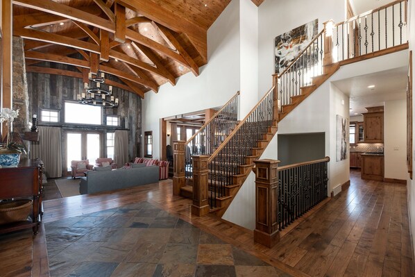 A spacious living area with a wooden staircase, large windows, and a high ceiling.