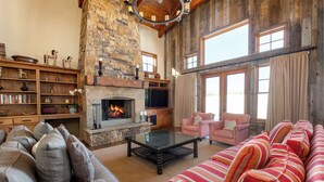 A cozy living room with a stone fireplace, a television, and a striped sofa. - Managed by Park City Lodging-Private Home with Stunning Deer Valley Resort Views (Park City)
