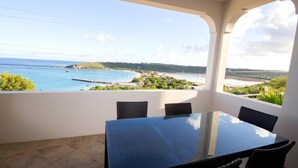 Een balkon met een glazen tafel en stoelen, met uitzicht op de kust onder een heldere lucht.