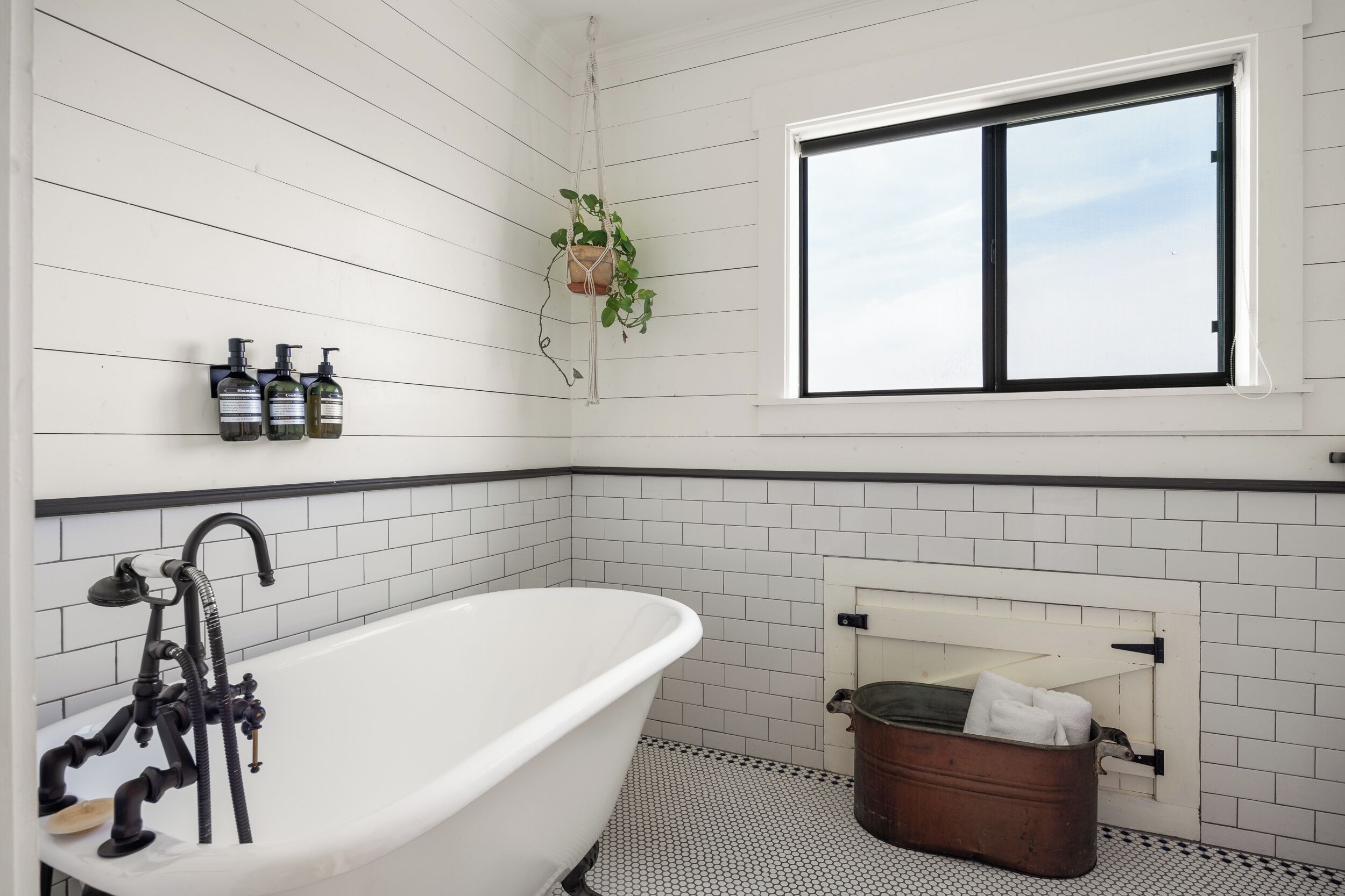 A bathroom with a freestanding bathtub, a window, and a hanging plant.