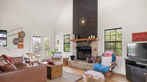 A spacious living room with a stone fireplace, leather sofa, and a television.