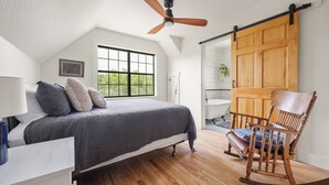 A bedroom with a bed, a rocking chair, a ceiling fan, a window, and a sliding barn door.