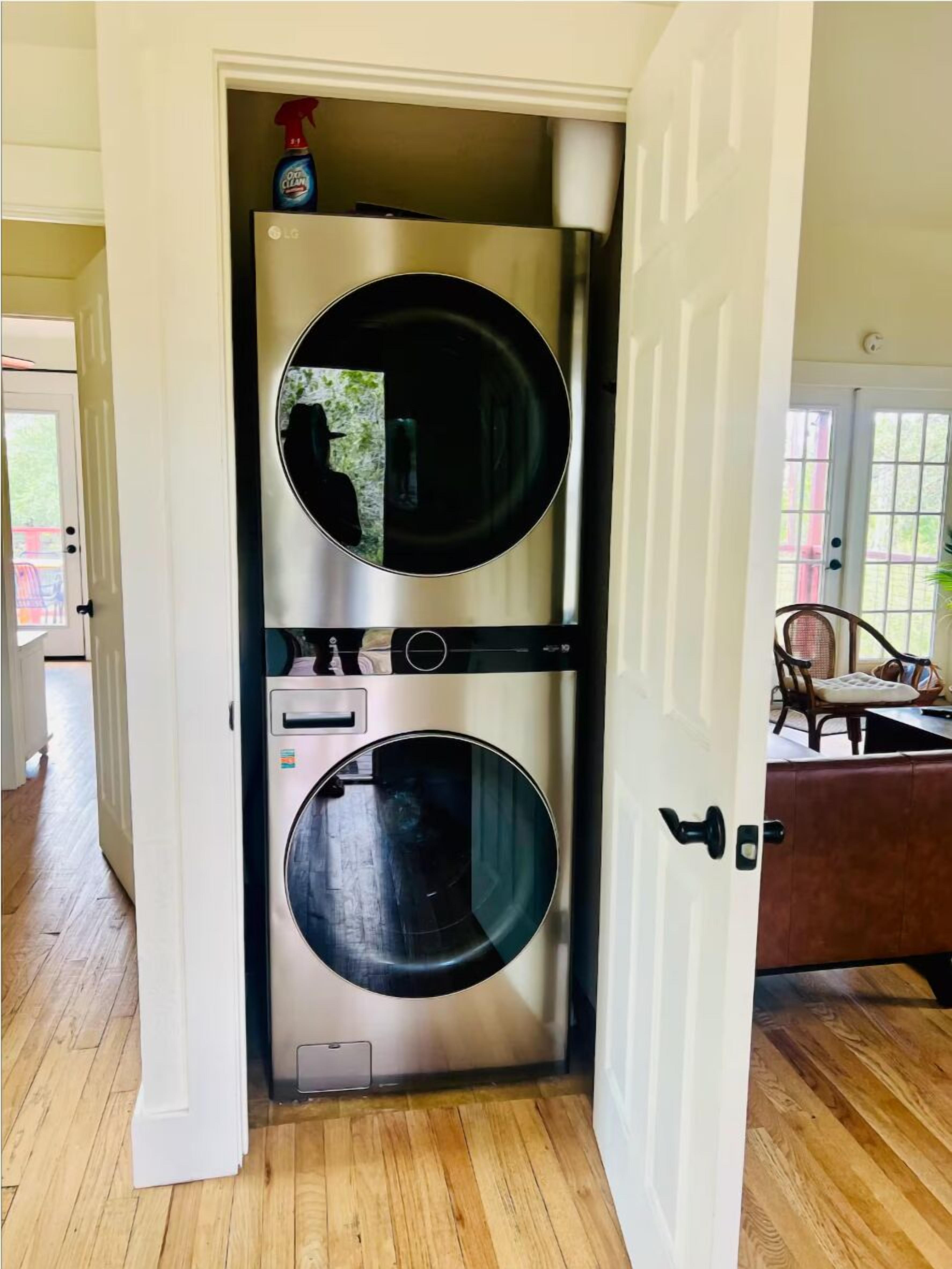 A compact, built-in washer and dryer unit with a control panel, located in a hallway with wooden flooring and a door leading to another room.