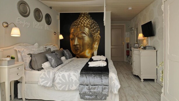 A bedroom with a large Buddha mural, a white bed, and a TV on the wall. - B&B de Valkenhorst (Lelystad)