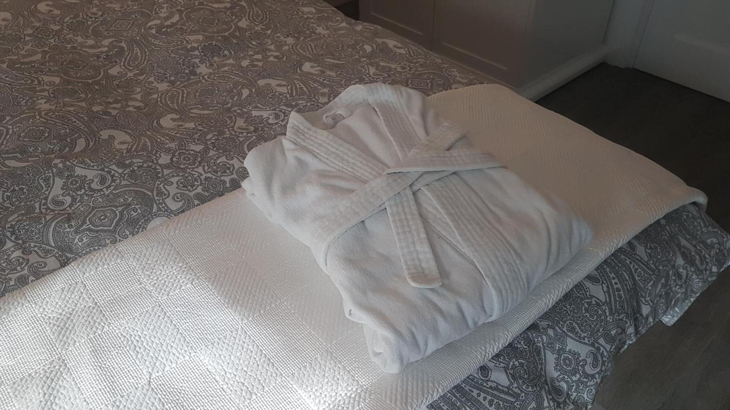 Un letto rifatto con cura, una coperta a motivi decorativi, un cuscino bianco e un accappatoio piegato sul letto.