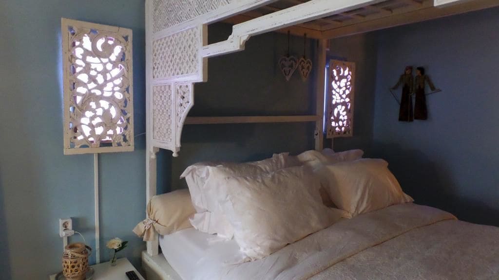 A bedroom with a bed, a nightstand, a decorative wall panel, and a wall-mounted shelf.