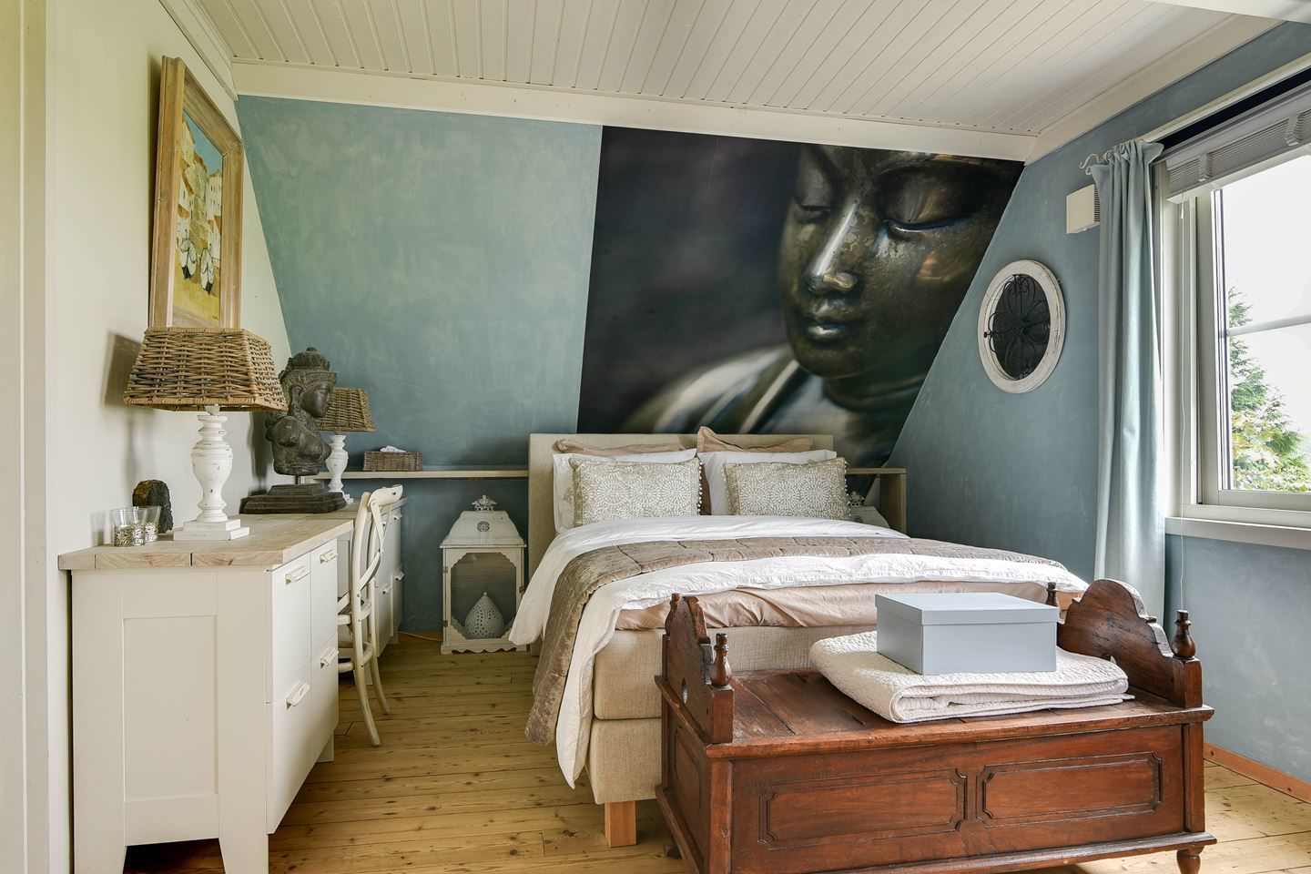 A bedroom with a bed, a dresser, a lamp, and a wall mural.