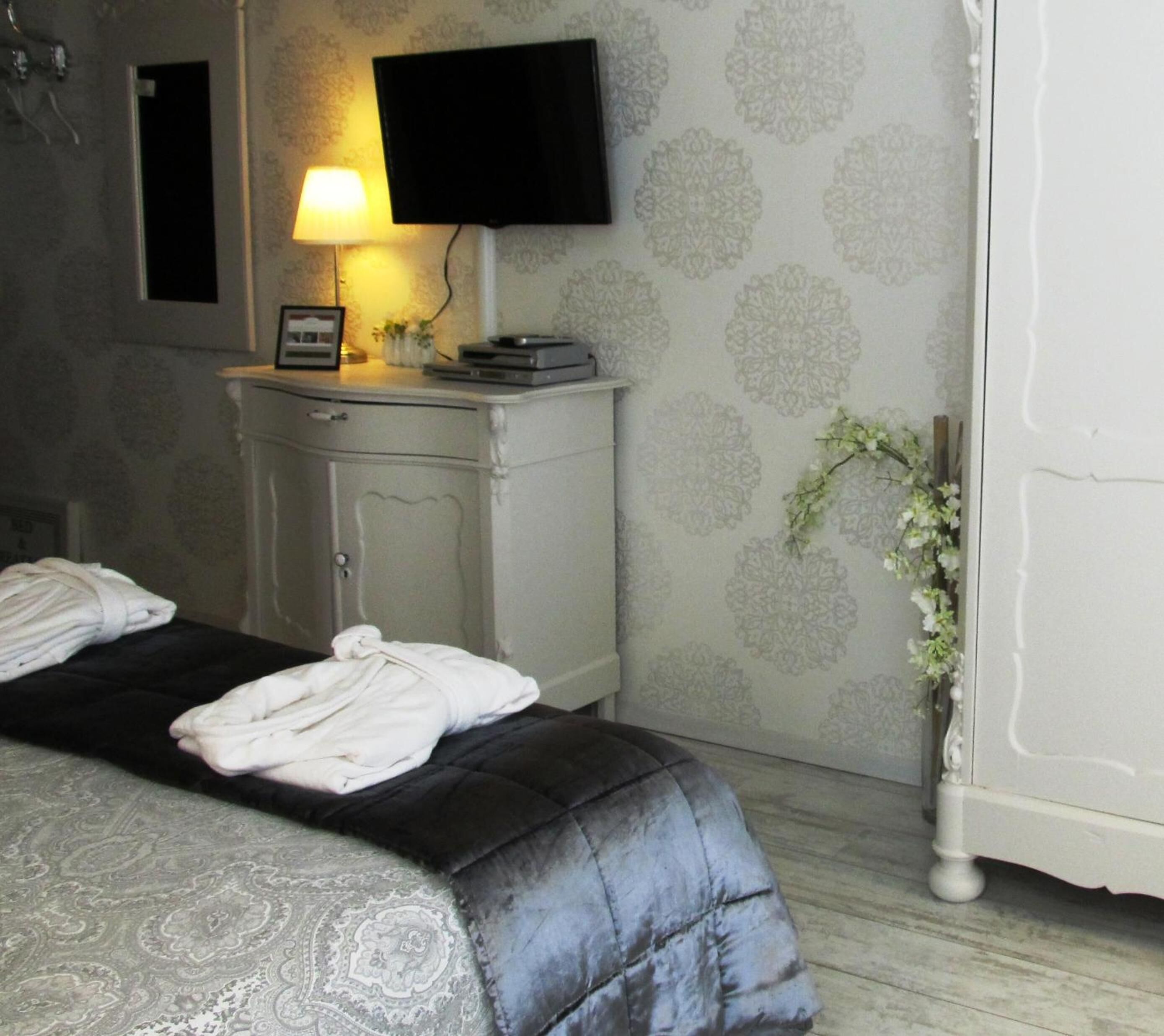 A hotel room with a bed, a nightstand, a television, and a wall-mounted lamp.
