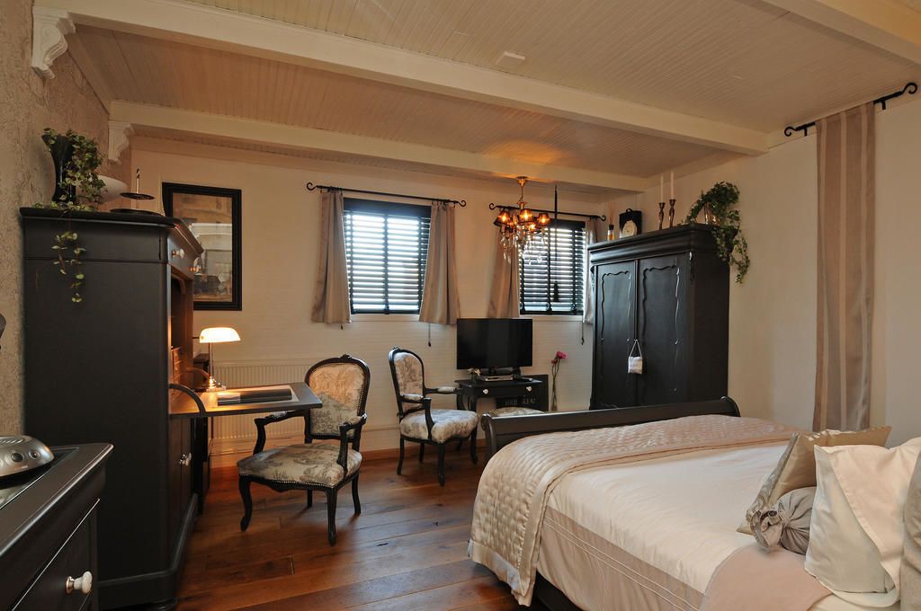 A hotel room with a bed, a desk with a lamp, two chairs, a television, and a wardrobe.